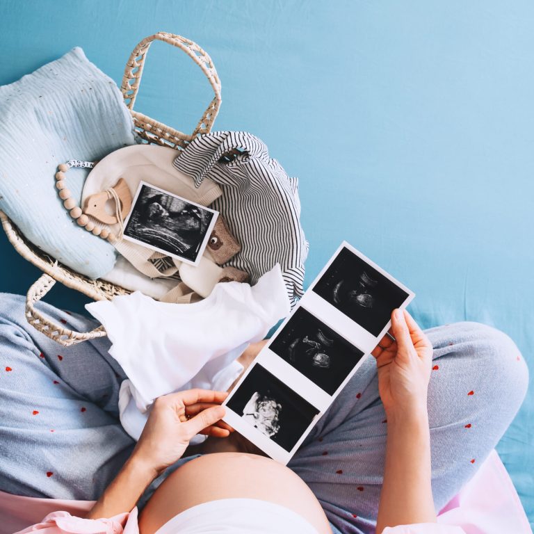 Pregnant woman looking at ultrasound images. Expectant mother waiting and preparing for baby birth during pregnancy. Mother with wicker basket of stuff for newborn child.